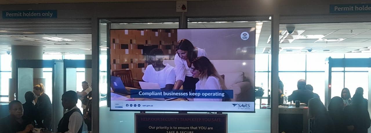 SARS ad on a large indoor screen above a security checkpoint at Cape Town International Airport